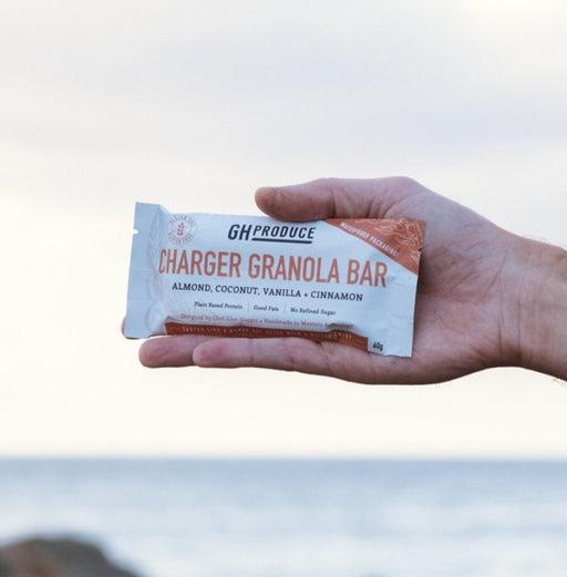 Hand holding a protein bar with ocean and rocks in the background