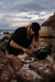 Person preparing food on a rocky beach with ocean and sky in the background