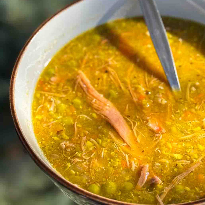 Close-up of a bowl of soup with a spoon, blurred green background